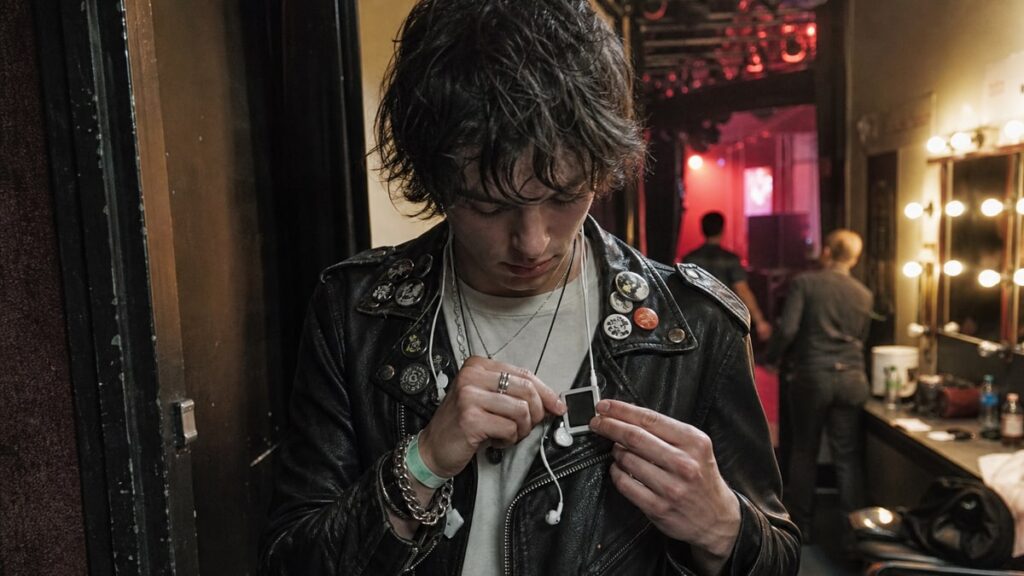 Why the iPod Shuffle Is Suddenly Popular Again? Concertgoer clips a small music player to a leather jacket in a backstage hallway